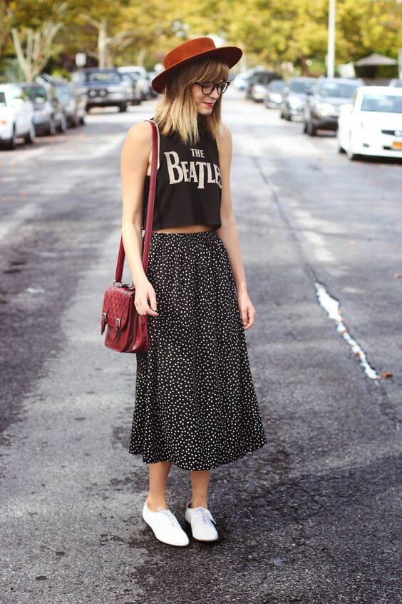 Chica con falda de topos, camiseta negra, sombrero y bolso.