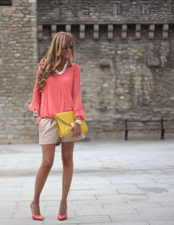 Chica con short beige y blusa living coral con clutch mostaza.